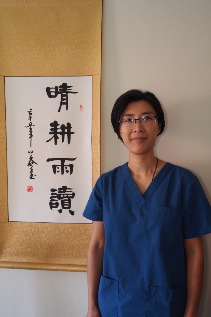 Rachel Cheng, TCM Teacher, next to a Chinese Banner